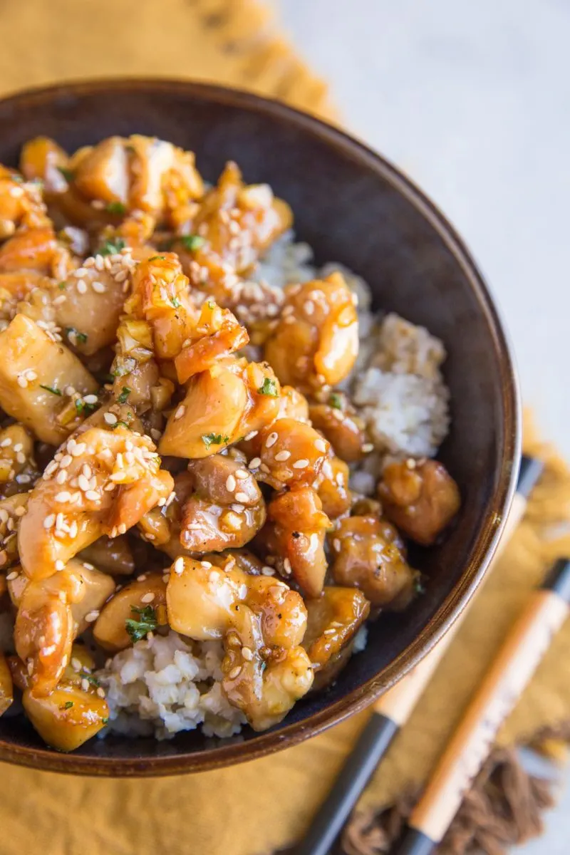 bowl of honey garlic chicken sitting on a golden napkin with chopsticks to the side