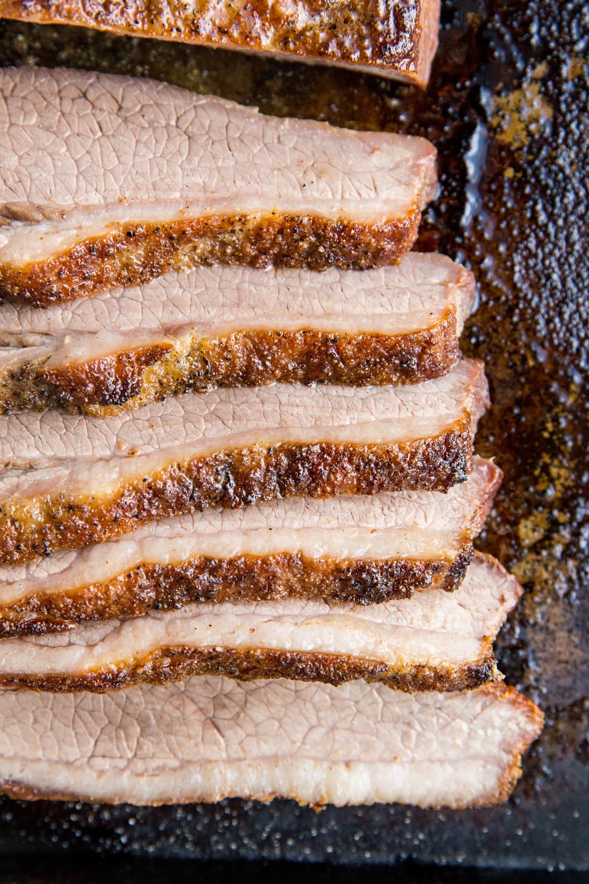 Top down photo of many slices of beef brisket on a baking sheet