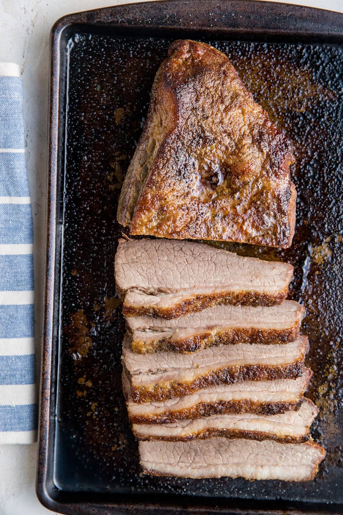 Whole brisket in slices on a baking sheet with blue striped napkin next to it