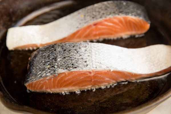 Salmon filets flesh side down in a skillet to become crispy.