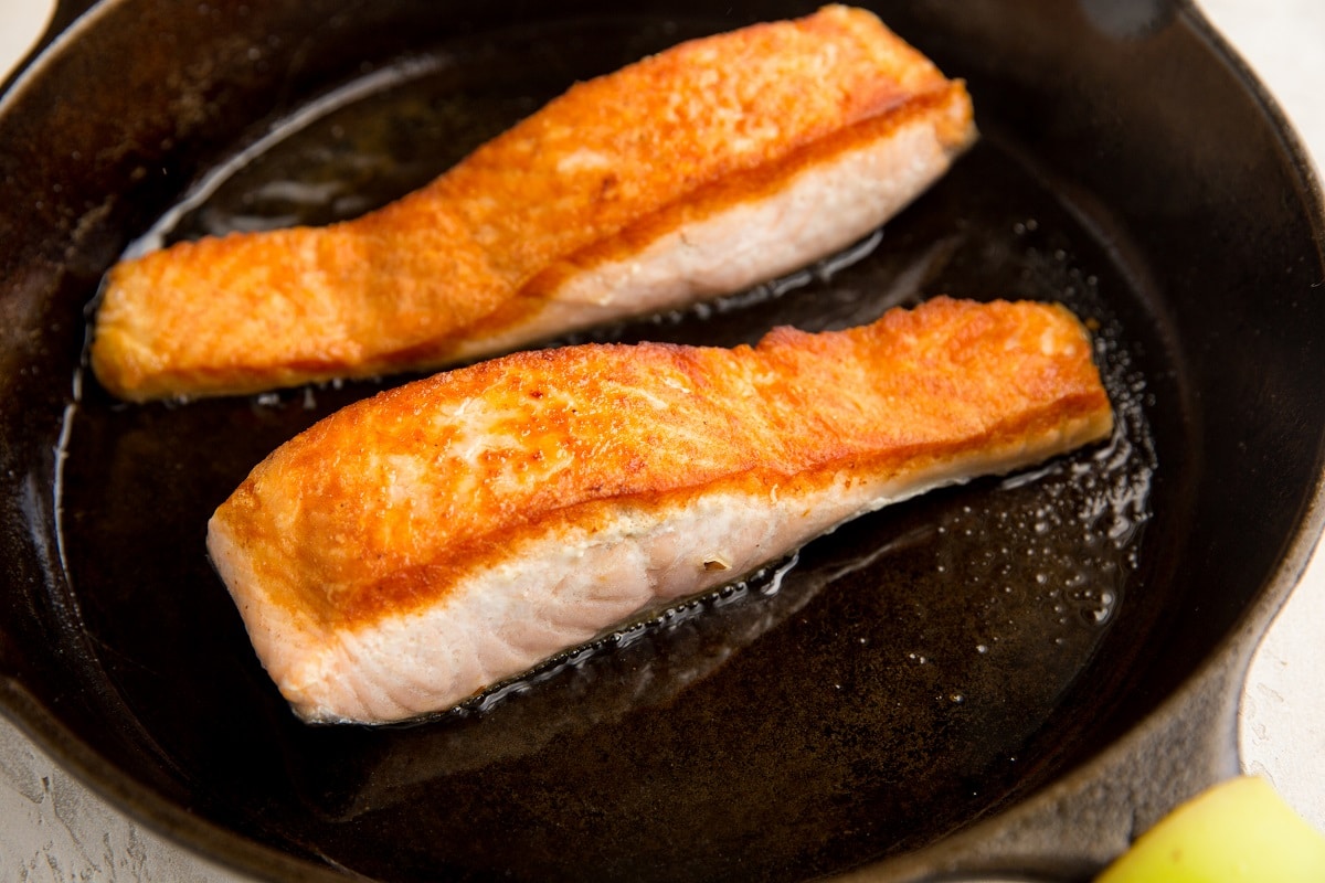 salmon filets cooking in a cast iron skillet