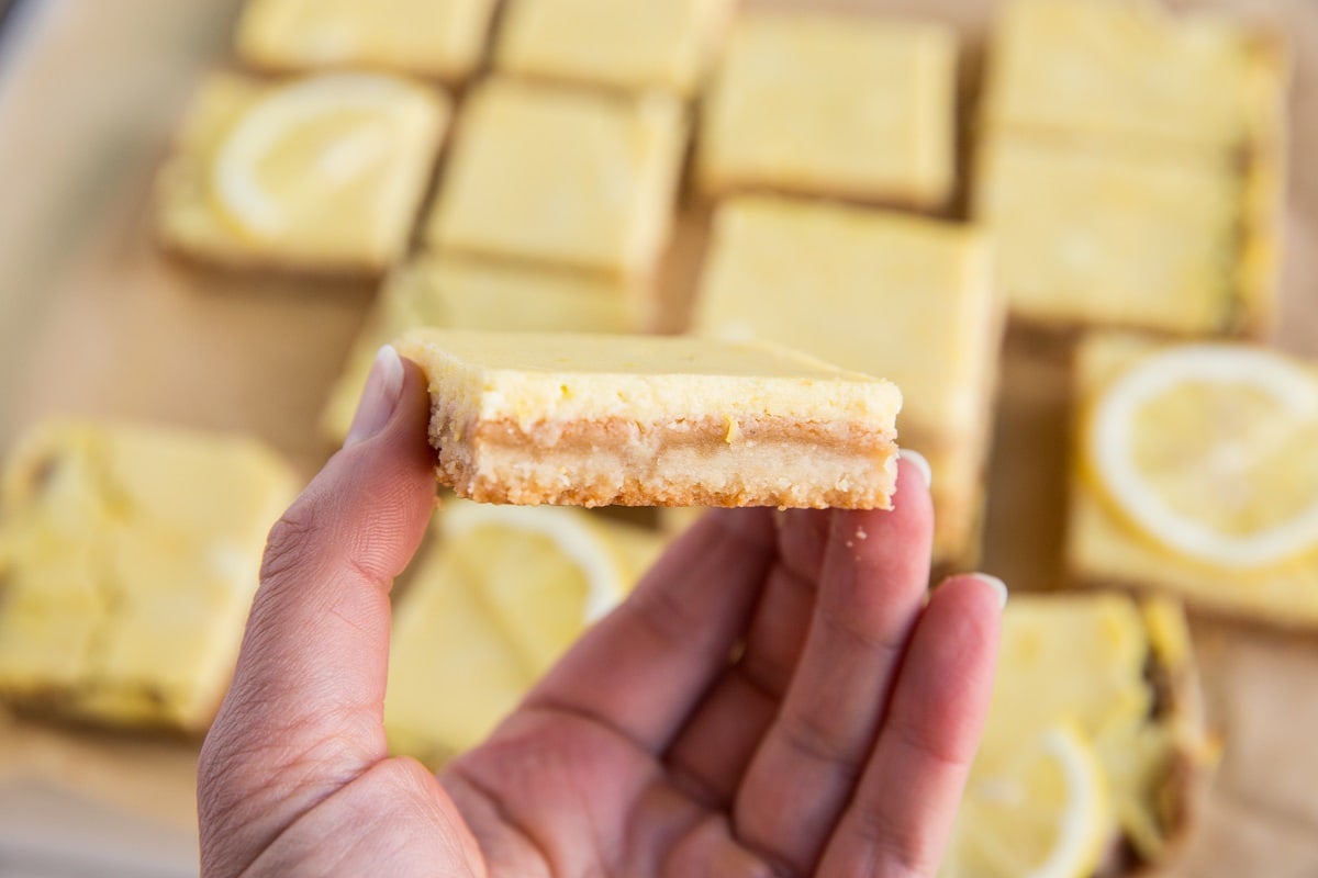 Hand holding a low carb lemon bar with lemon bars in the background