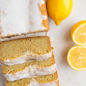 Top down photo of a loaf of lemon pound cake that has been cut into slices. Fresh lemons to the side