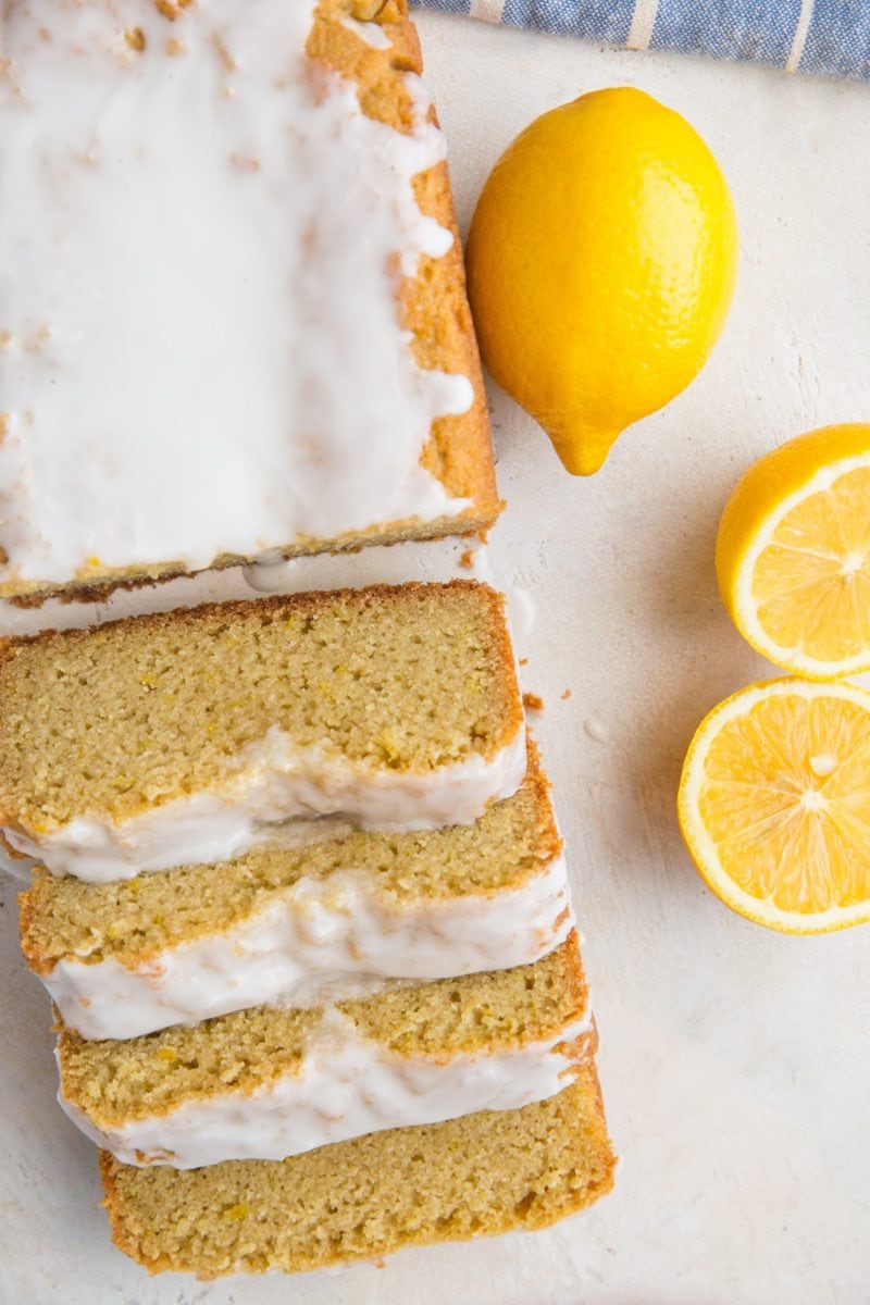 Top down photo of a loaf of lemon pound cake that has been cut into slices. Fresh lemons to the side