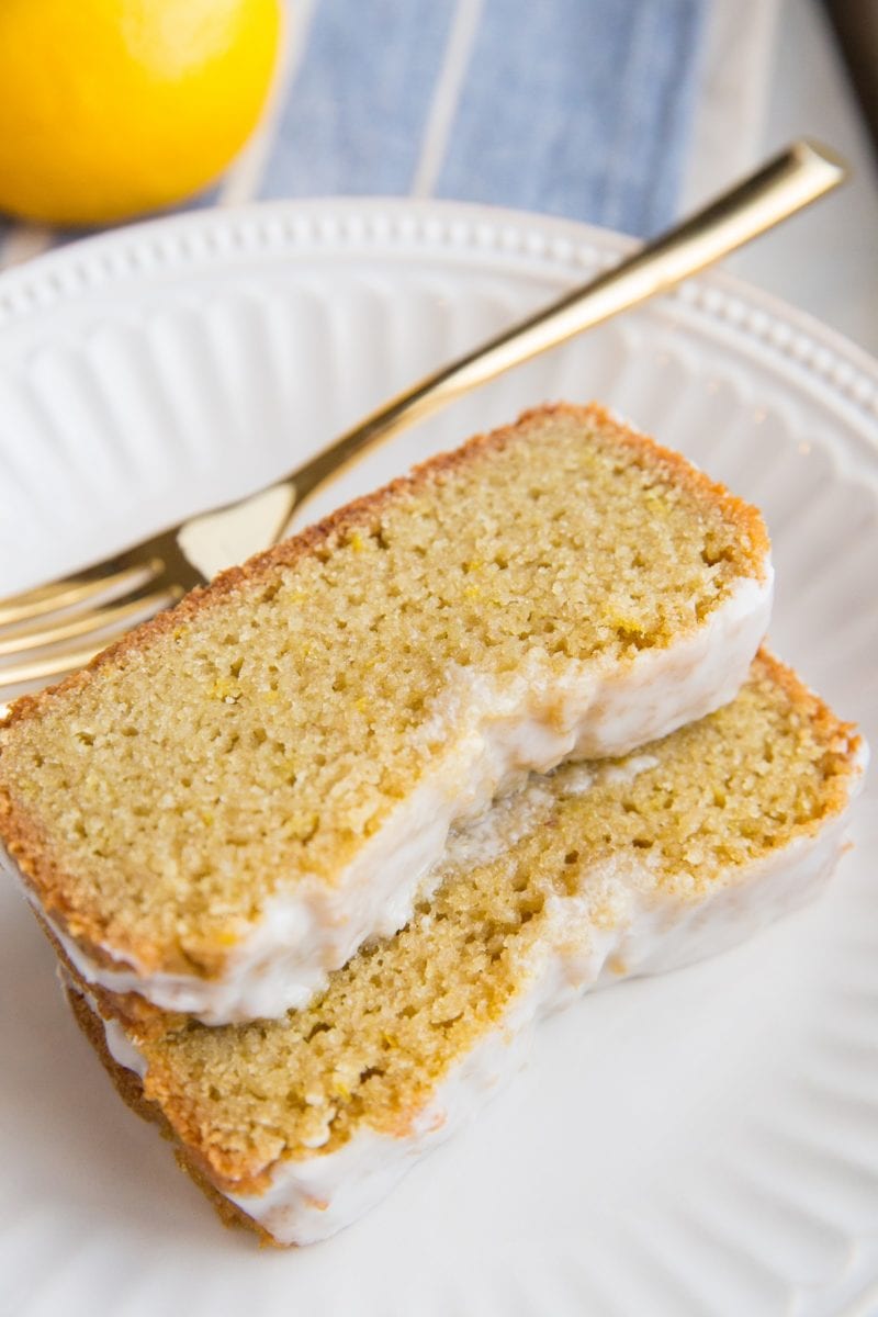 White plate with two thick slices of low-carb lemon pound cake with a gold fork and a blue napkin