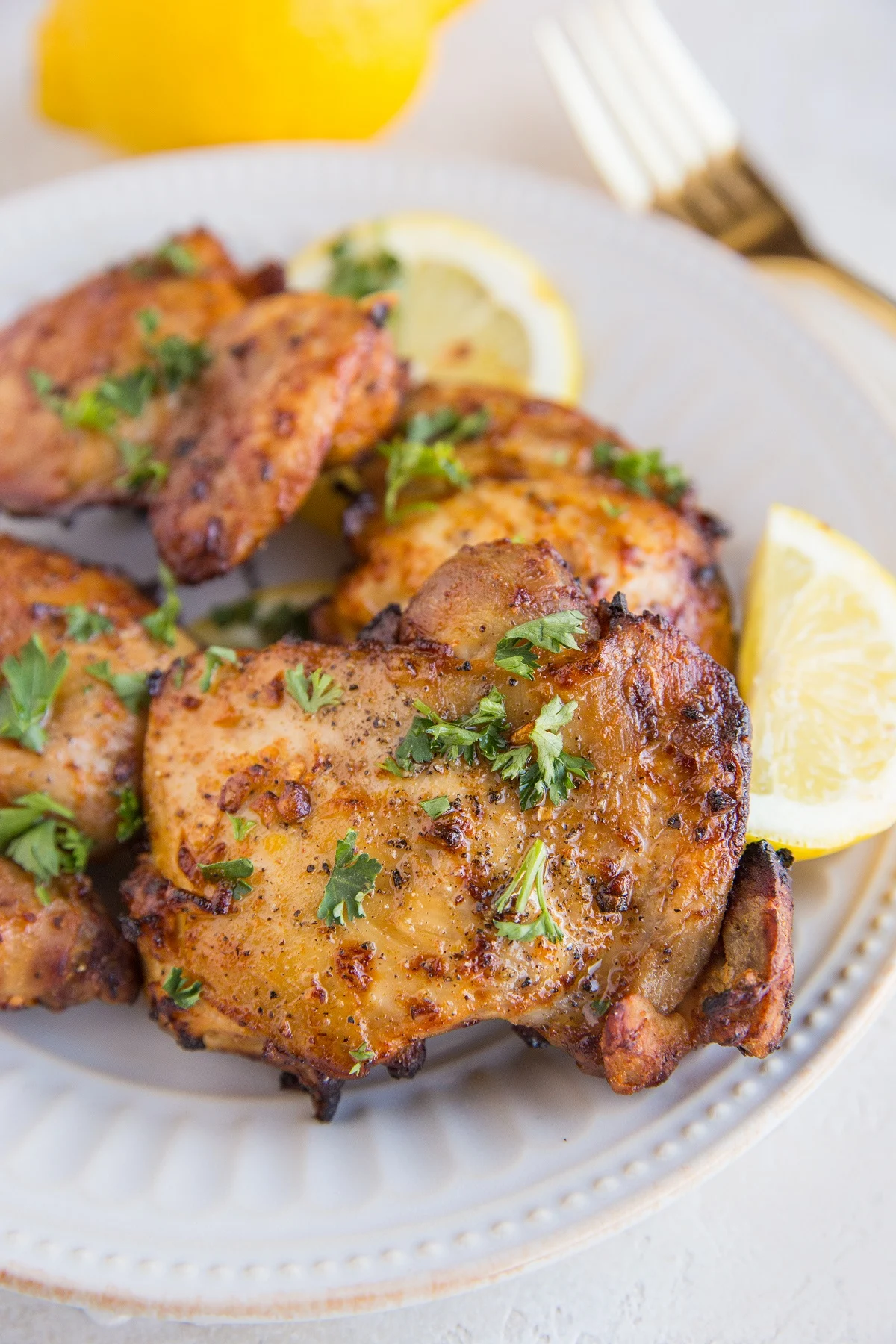 Lemon garlic chicken thighs on a white plate sprinkled with parsley and a slice of lemon