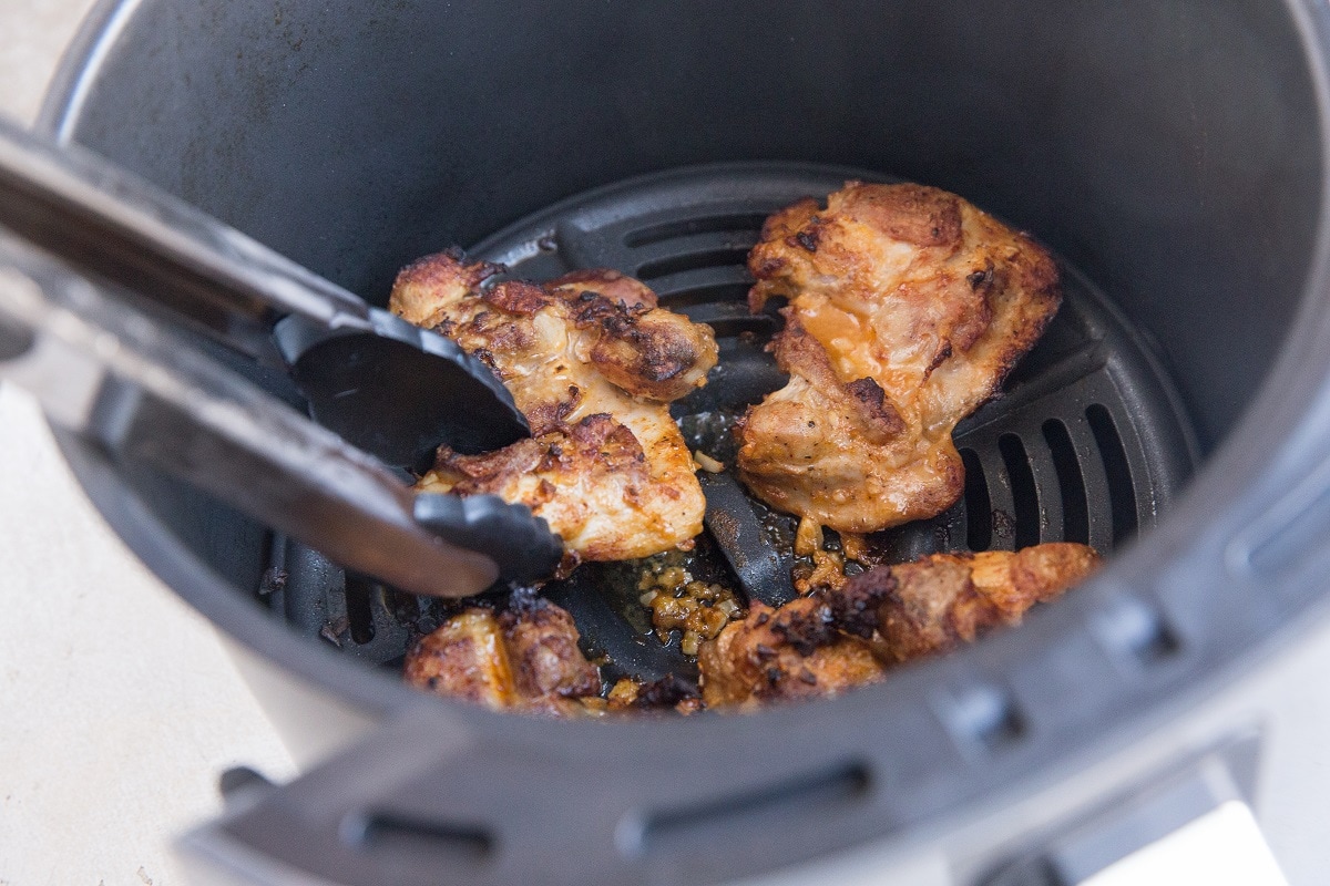 Tongs flipping chicken thighs in an air fryer
