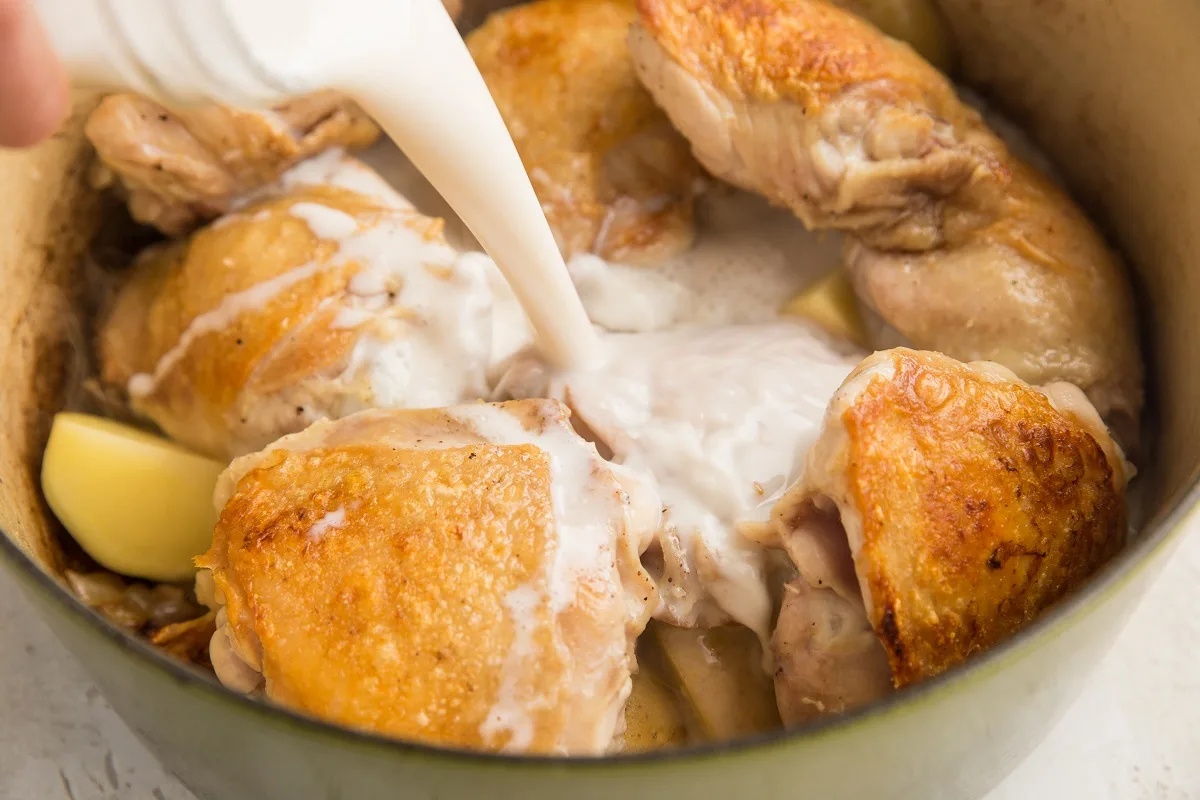 Chicken and potatoes in a dutch oven and pouring in coconut milk