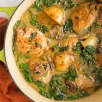 Top down photo of a green Dutch oven full of chicken and potatoes with a red napkin to the side