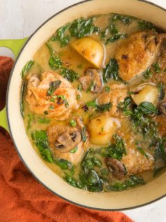 Top down photo of a green Dutch oven full of chicken and potatoes with a red napkin to the side