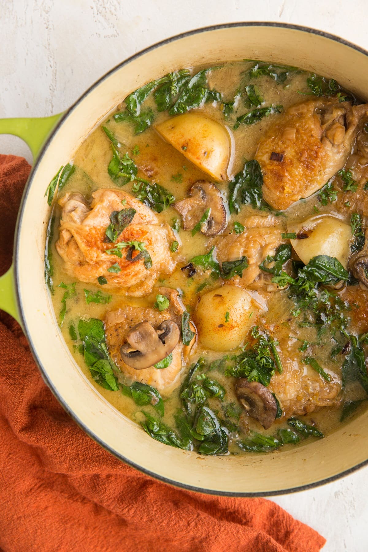 Top down photo of a green Dutch oven full of chicken and potatoes with a red napkin to the side