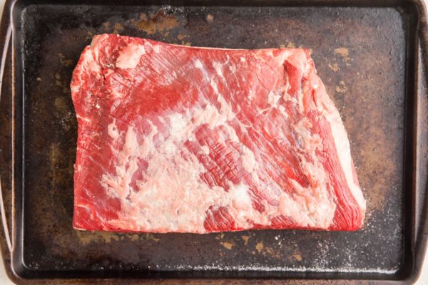 Beef brisket on a baking sheet sprinkled with sea salt for dry brining