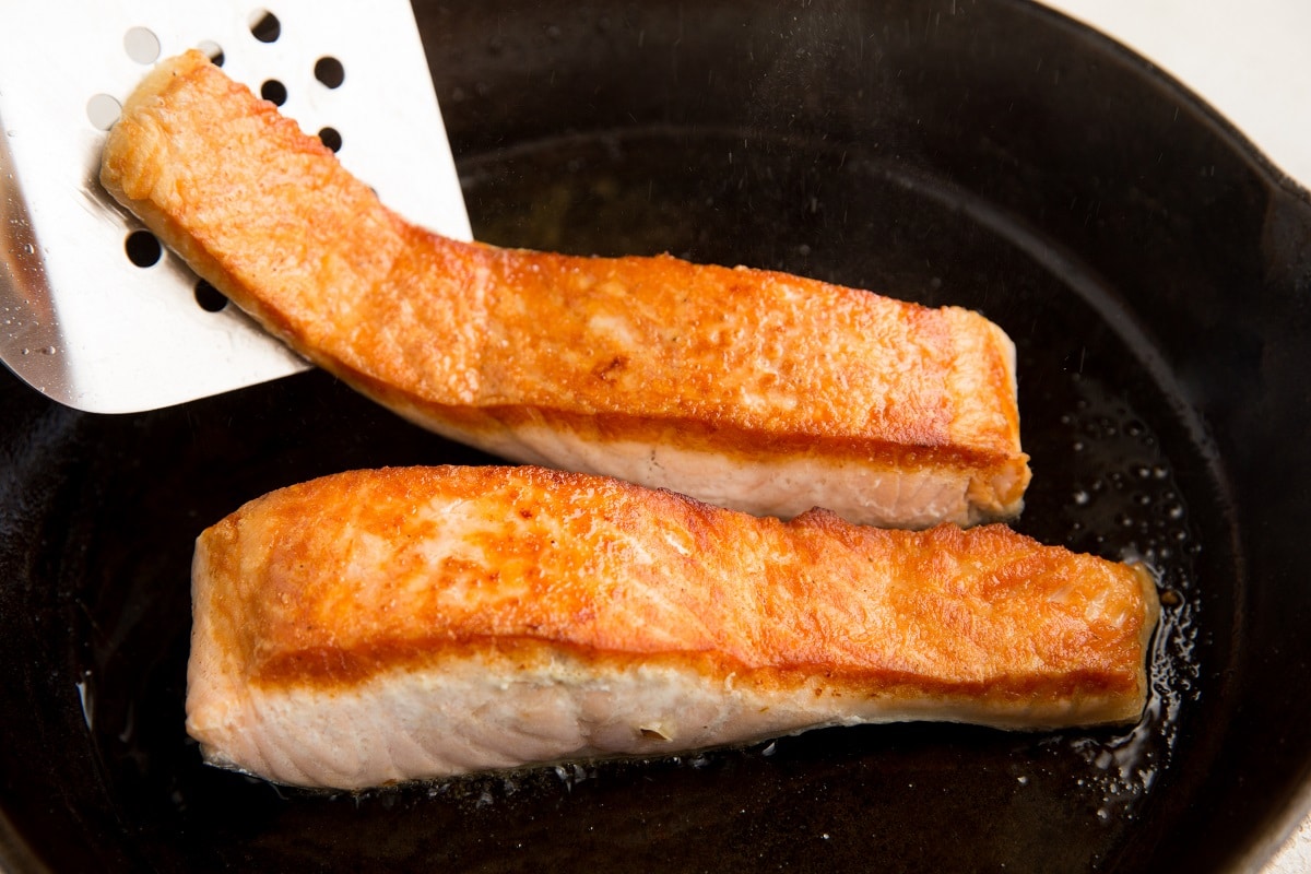 Flipping salmon filets in a cast iron skillet with a metal spatula