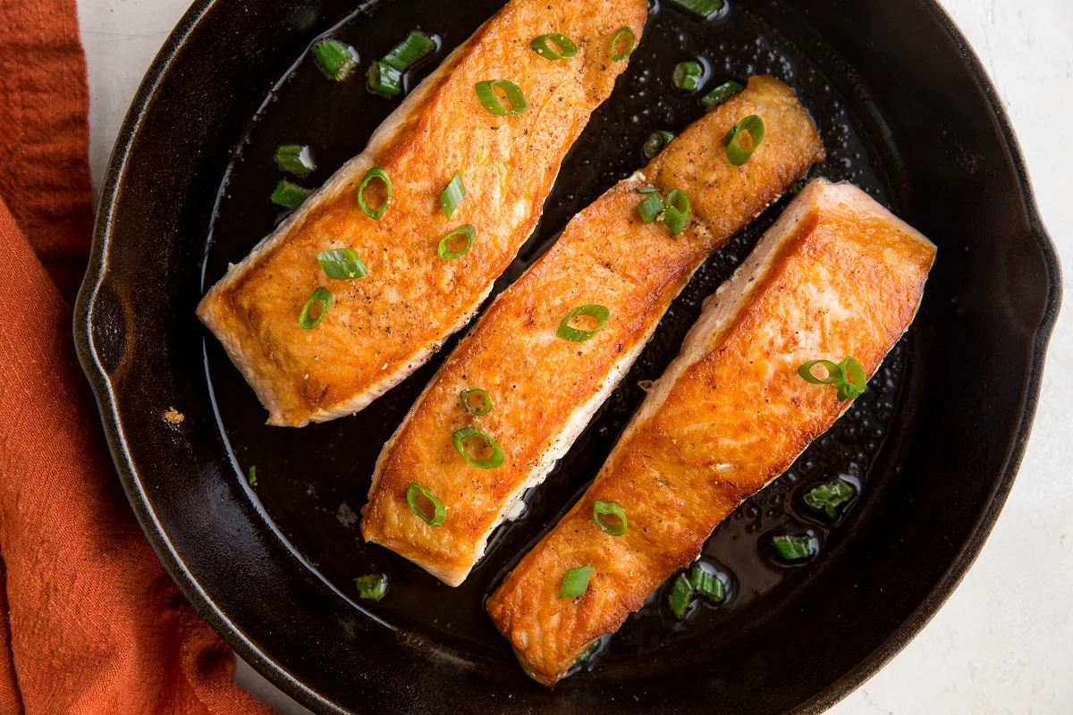horizontal photo of cast iron skillet with three crispy skillet cooked salmon filets