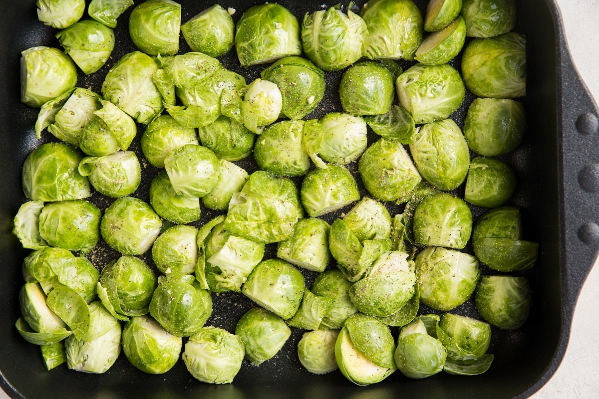 Brussel sprouts in a casserole dish with oil and seasonings ready to go into the oven
