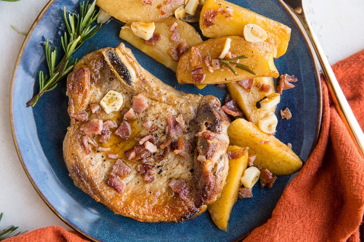 Horizontal photo of a roasted pork chop on a blue plate with a side of stewed apples and a red napkin