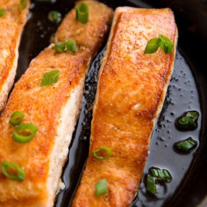Pan-seared salmon in a cast iron skillet with bits of green onion on top