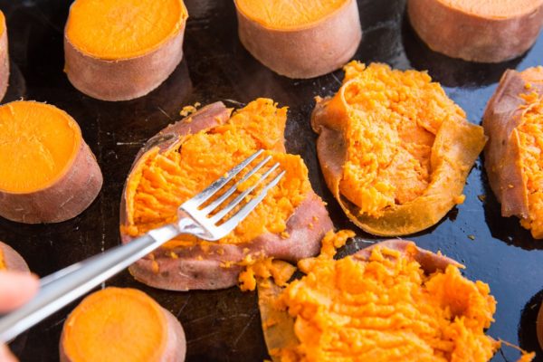 Cooked sweet potato rounds being mashed with a fork on a cookie sheet