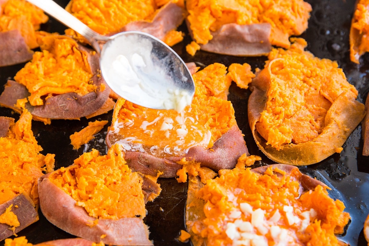 Smashed sweet potatoes being drizzled with garlic butter and honey