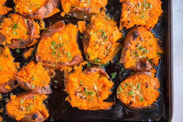 Finished smashed sweet potatoes on a baking sheet with butter garlic and fresh parsley