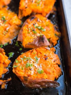 Sheet pan of smashed sweet potatoes with butter on top, garnished with fresh parsley