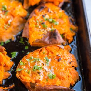 Sheet pan of smashed sweet potatoes with butter on top, garnished with fresh parsley