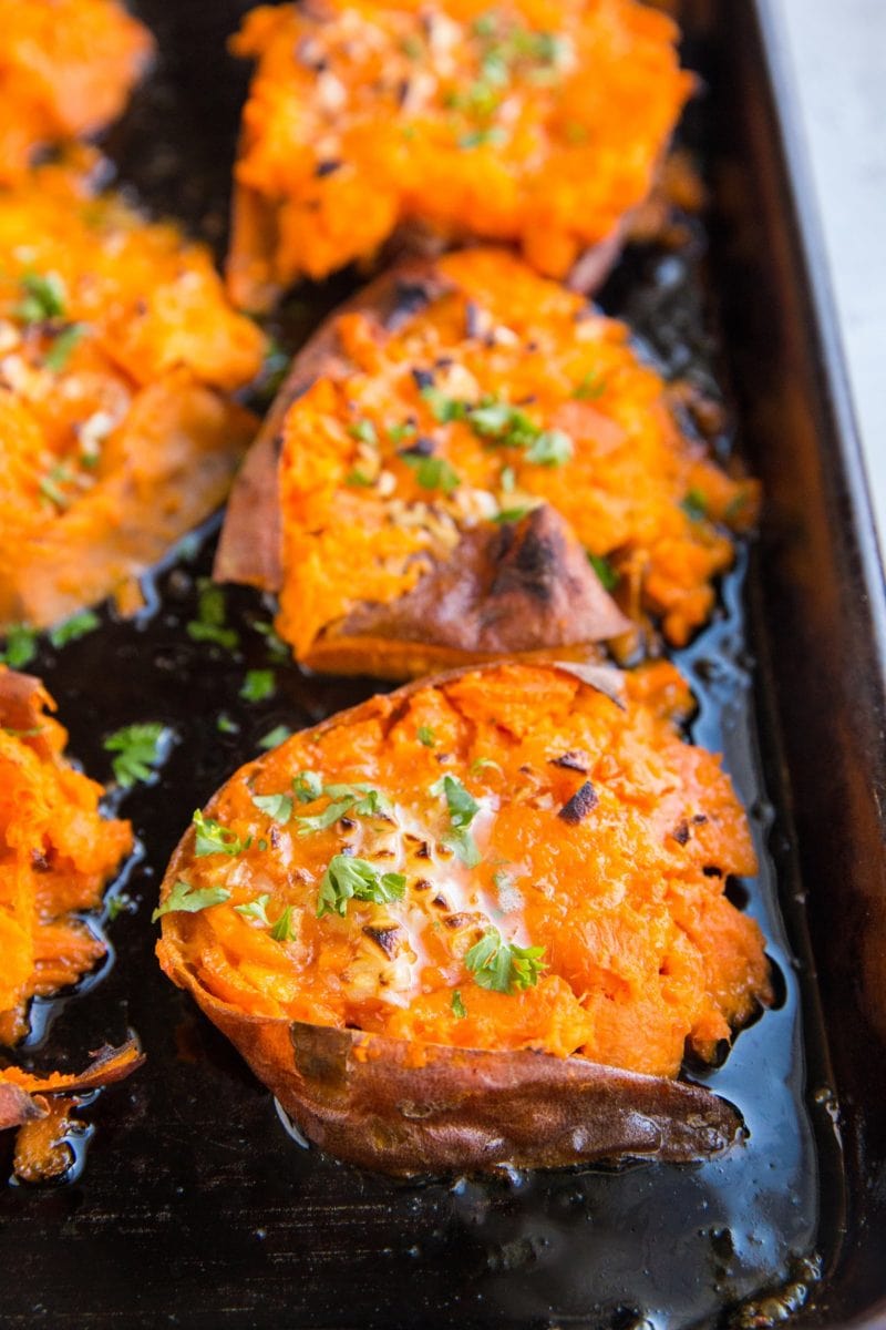 Sheet pan of smashed sweet potatoes with butter on top, garnished with fresh parsley