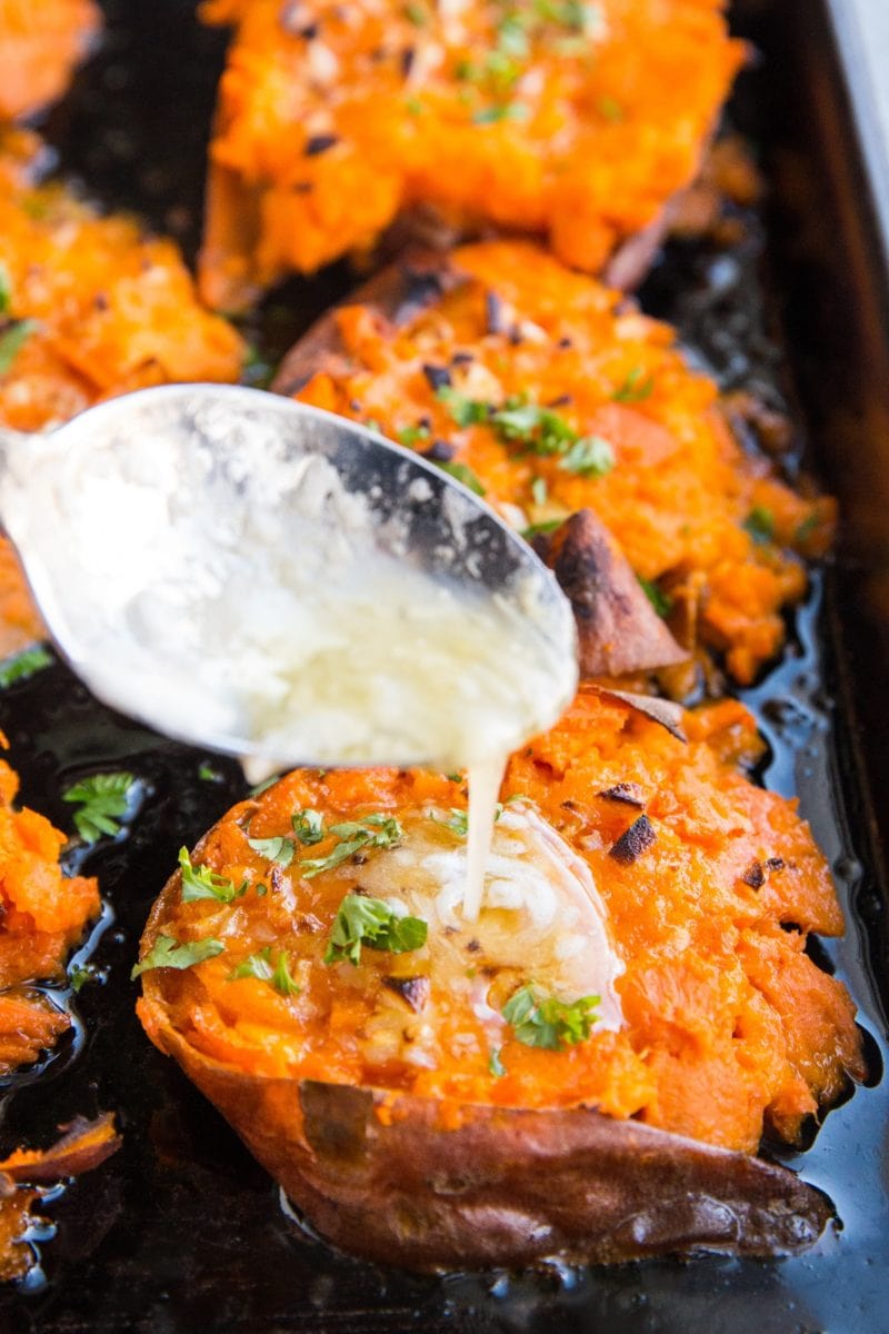 Mashed sweet potatoes on a baking sheet with butter being poured on top with a spoon