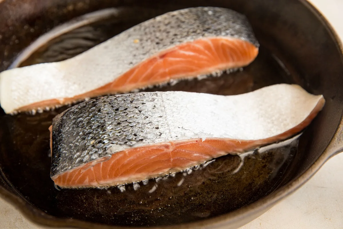 Salmon cooking flesh-side down in a cast iron skillet