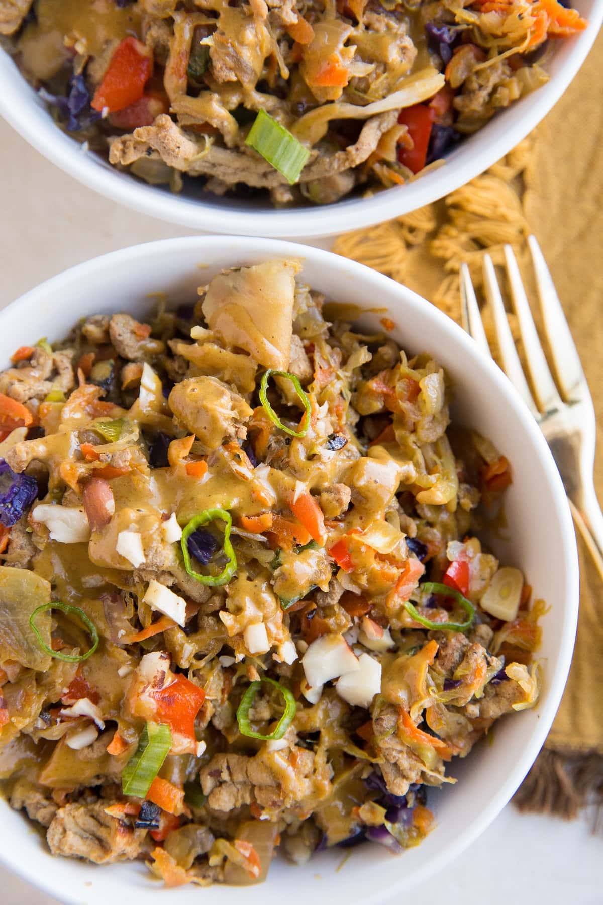 top down photo of two bowls of ground turkey cabbage bowls loaded with veggies and sauce with a fork and napkin to the side