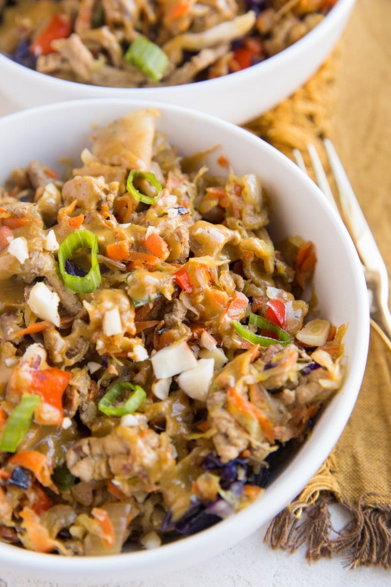 Two bowls of thai turkey and cabbage with veggies. A brown napkin and gold fork to the right of the bowls