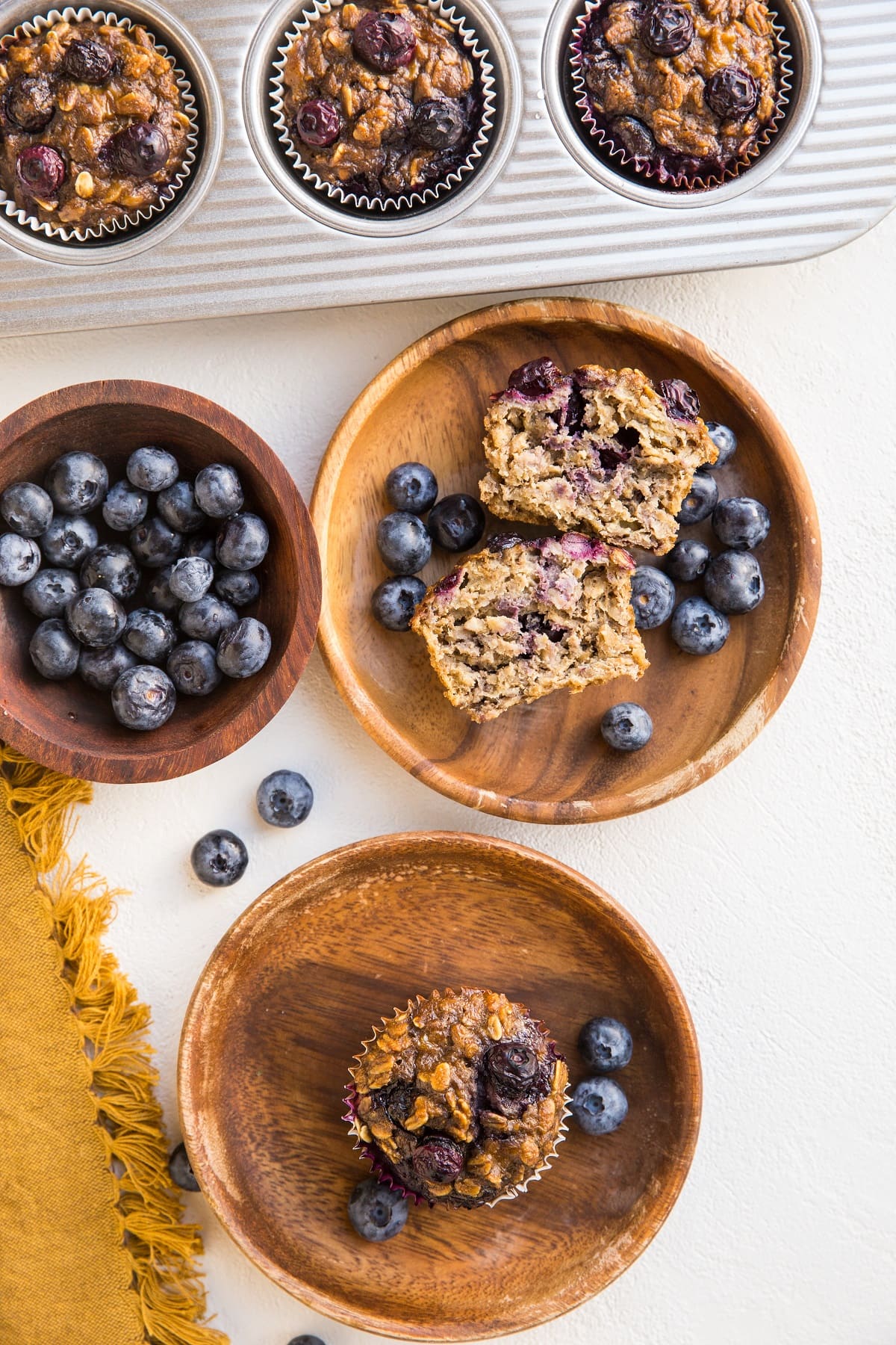 two plates of oatmeal muffins with the muffin tray and fresh berries to the side