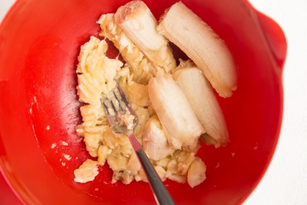 Fork mashing banana in a mixing bowl