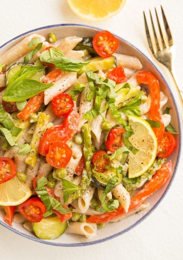 Top down photo of bowl of pasta primavera with a fork to the side and a lemon