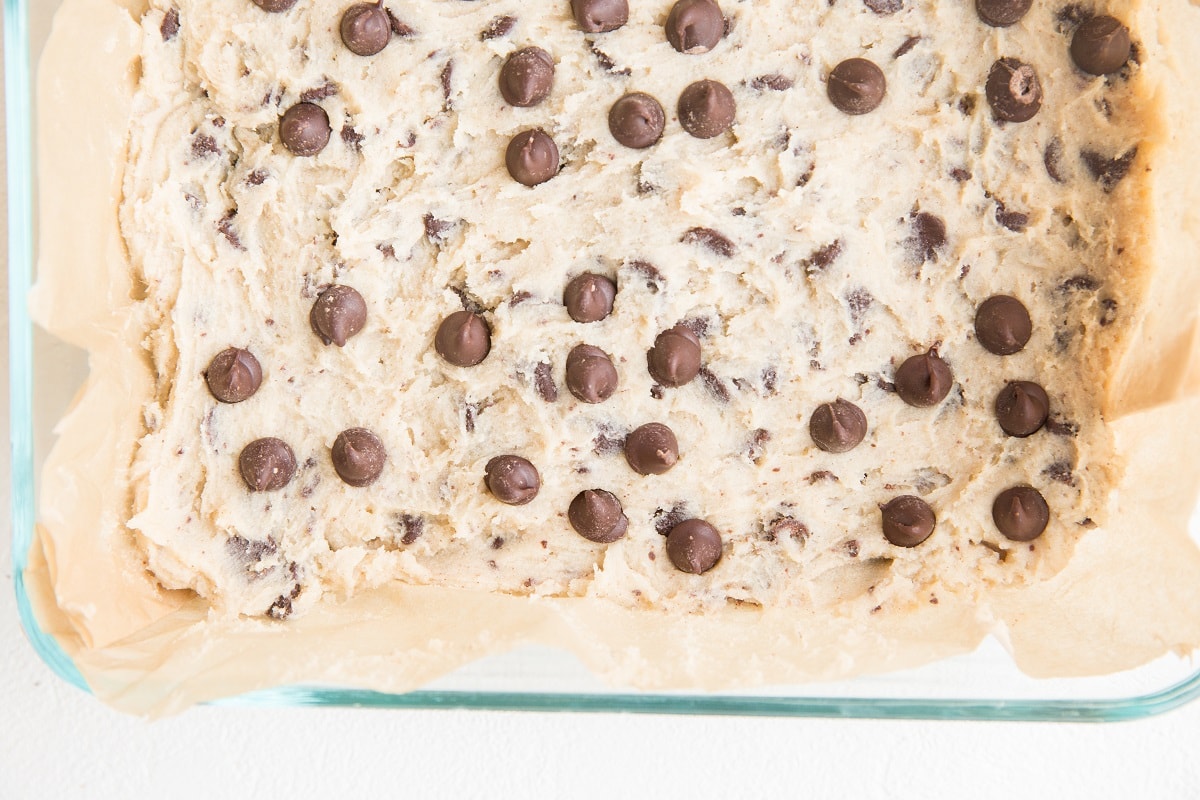 Baking dish with cookie dough spread over parchment paper