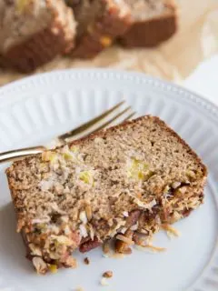 Slice of Grain-Free Hummingbird Bread on a plate with a loaf of bread in the background