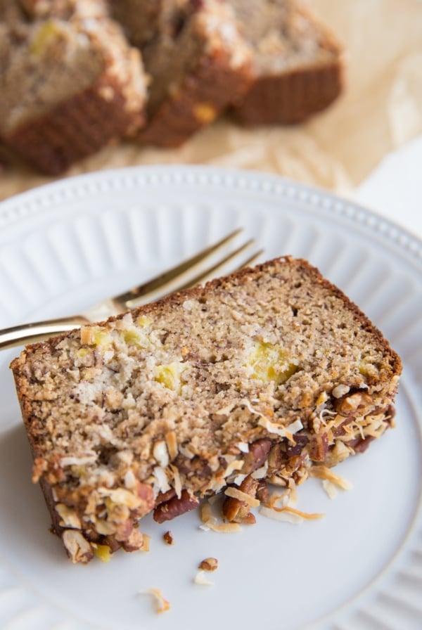 Slice of Grain-Free Hummingbird Bread on a plate with a loaf of bread in the background