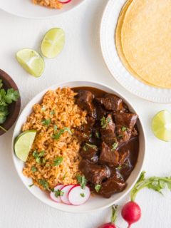 Bowl of chile colorado with Spanish rice and corn tortillas off to the side