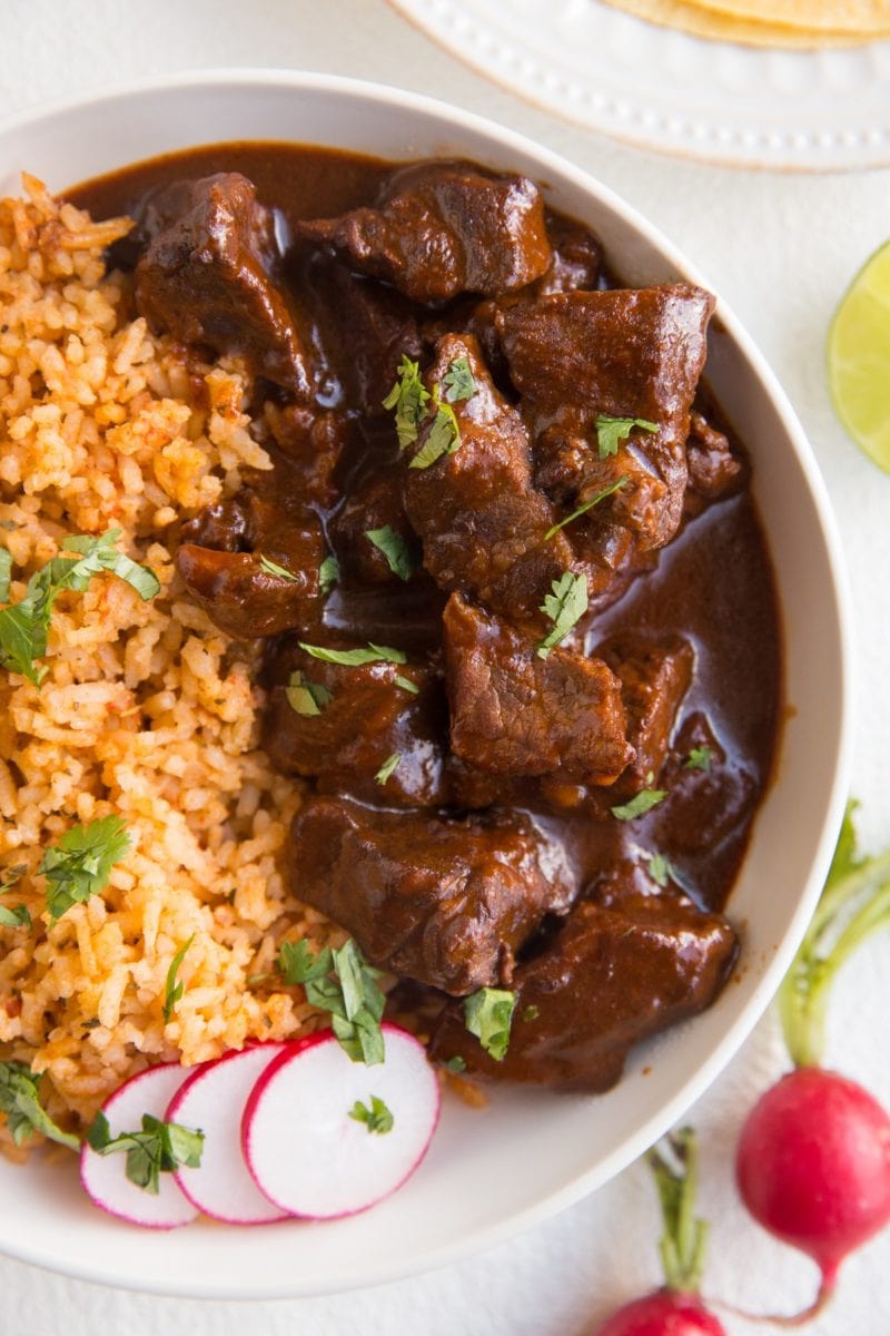 Close up top down image of chile colorado in a big bowl with Spanish rice and cilantro sprinkled on top