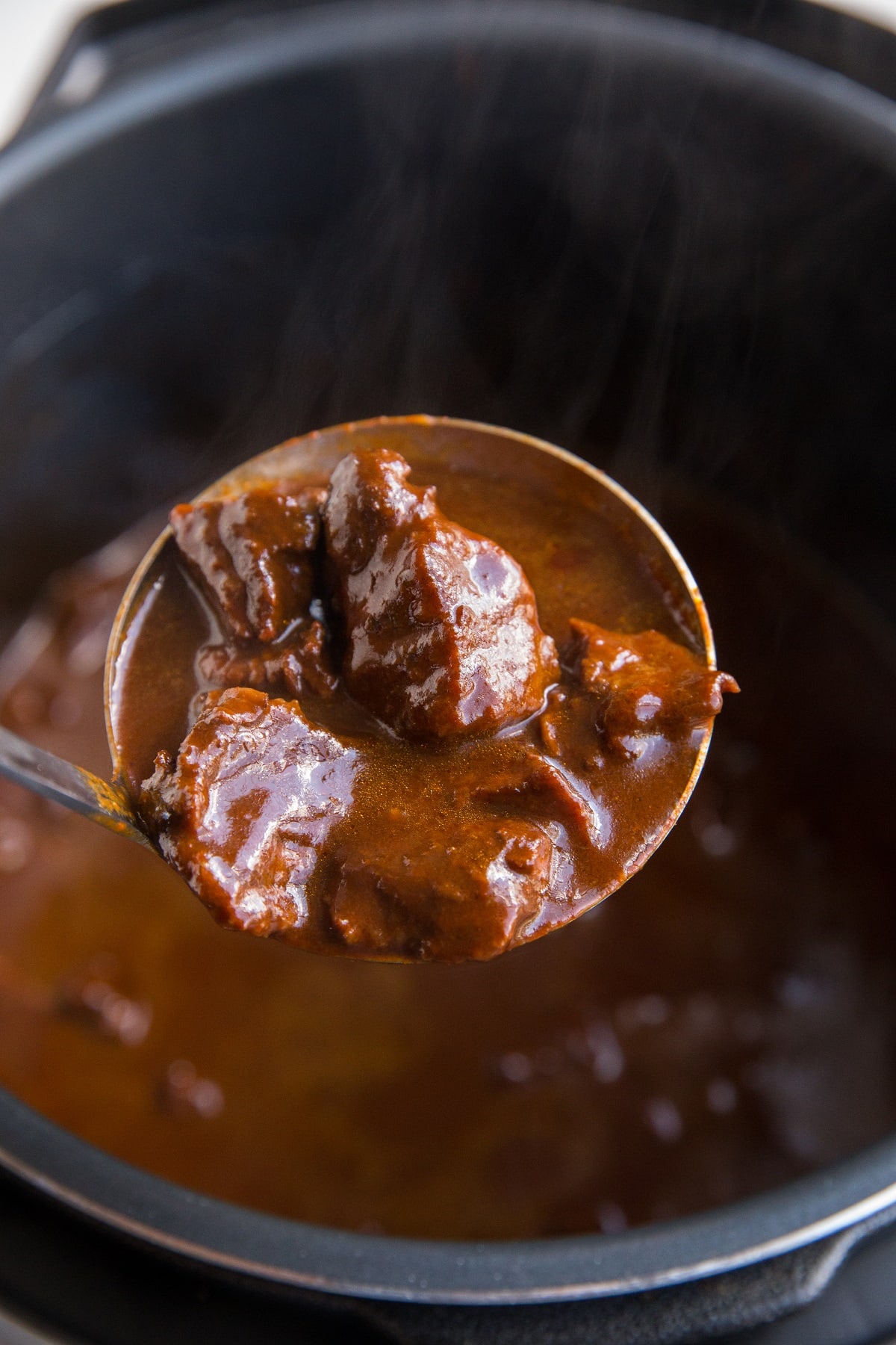 Pressure cooker with a ladle of chile colorado close to camera