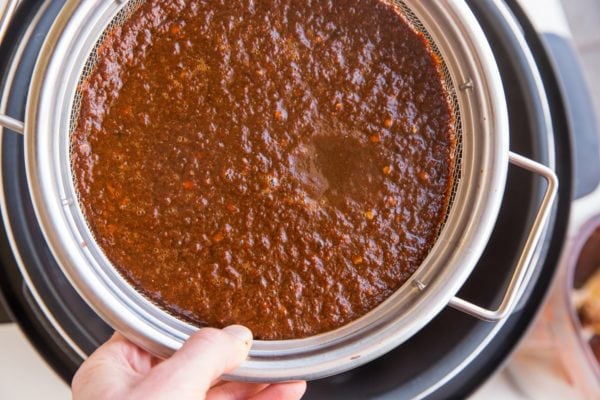 Strainer of chile colorado sauce hovering over an Instant Pot