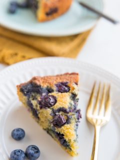 Two slices of keto blueberry cake on plates with fresh blueberries to the side and forks