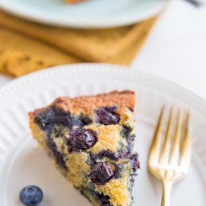 Two slices of keto blueberry cake on plates with fresh blueberries to the side and forks