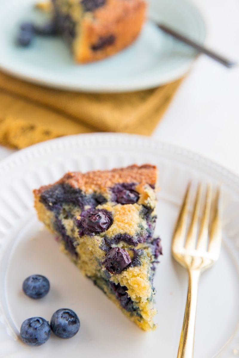 Two slices of keto blueberry cake on plates with fresh blueberries to the side and forks