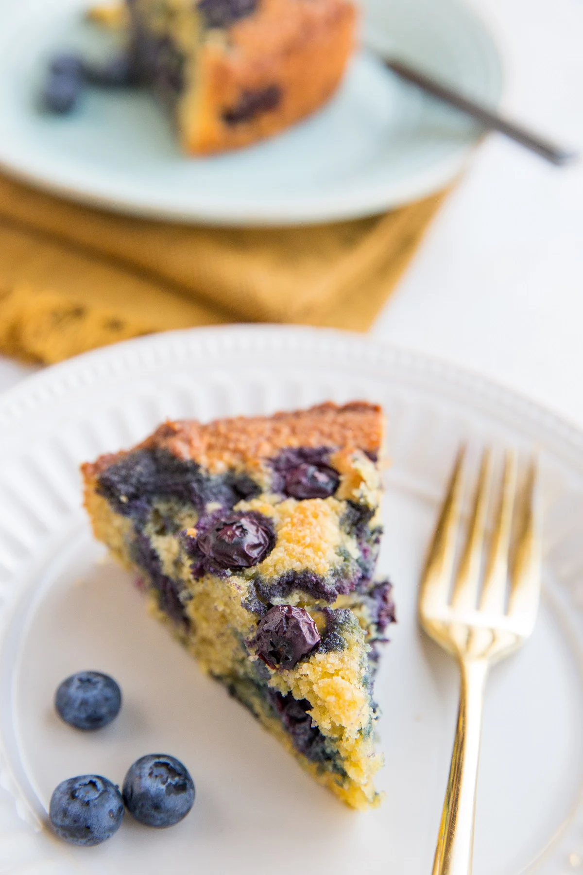 Two slices of keto blueberry cake on plates with fresh blueberries to the side and forks