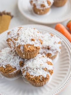 Keto Carrot Cake Muffins sitting on a plate with carrots in the background and another plate of muffins