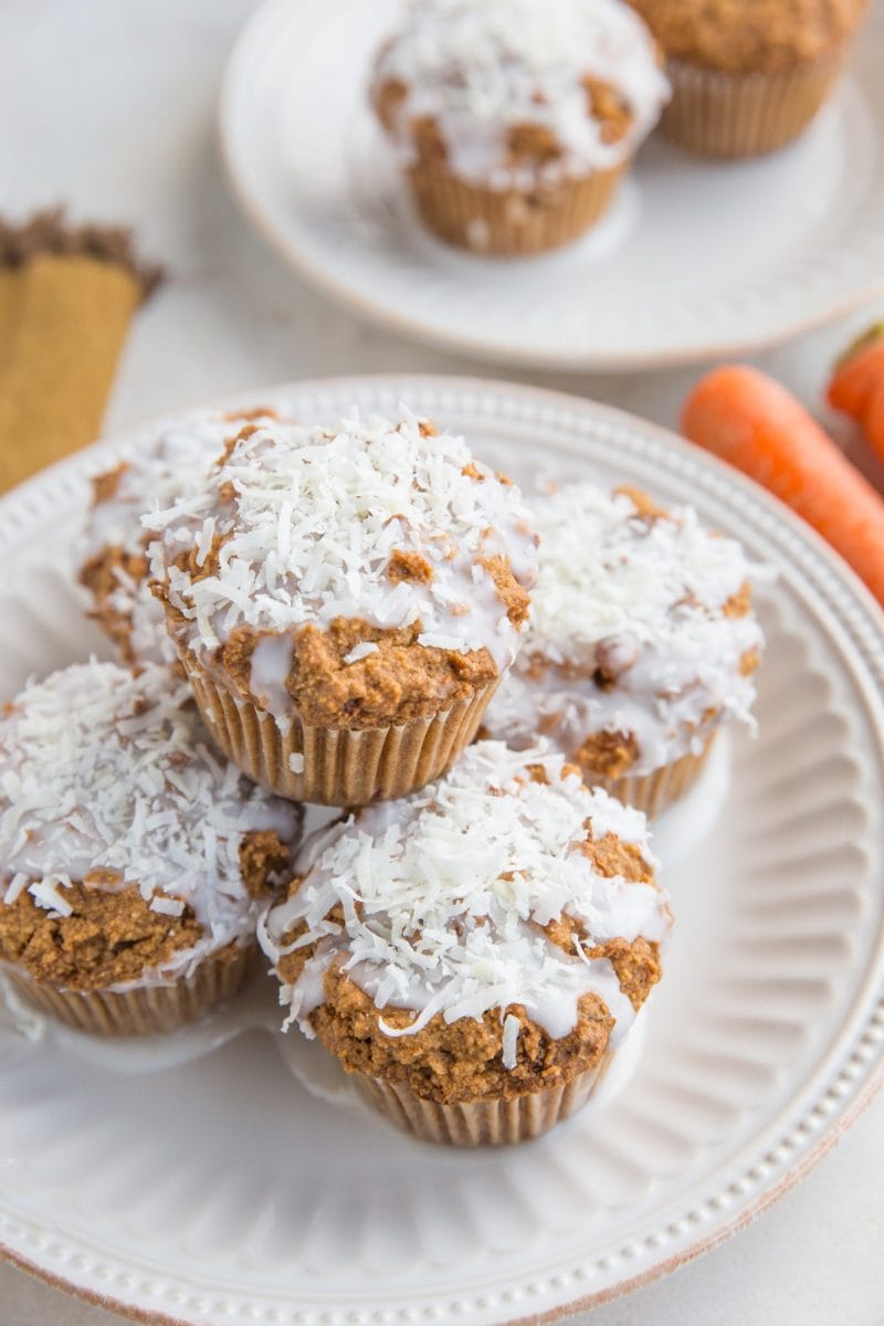 Keto Carrot Cake Muffins sitting on a plate with carrots in the background and another plate of muffins