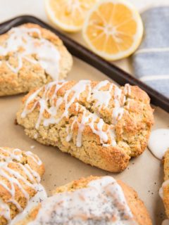 Lemon poppy seed scones on a baking sheet with lemons in the background