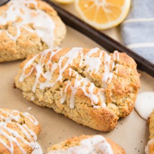 Lemon poppy seed scones on a baking sheet with lemons in the background