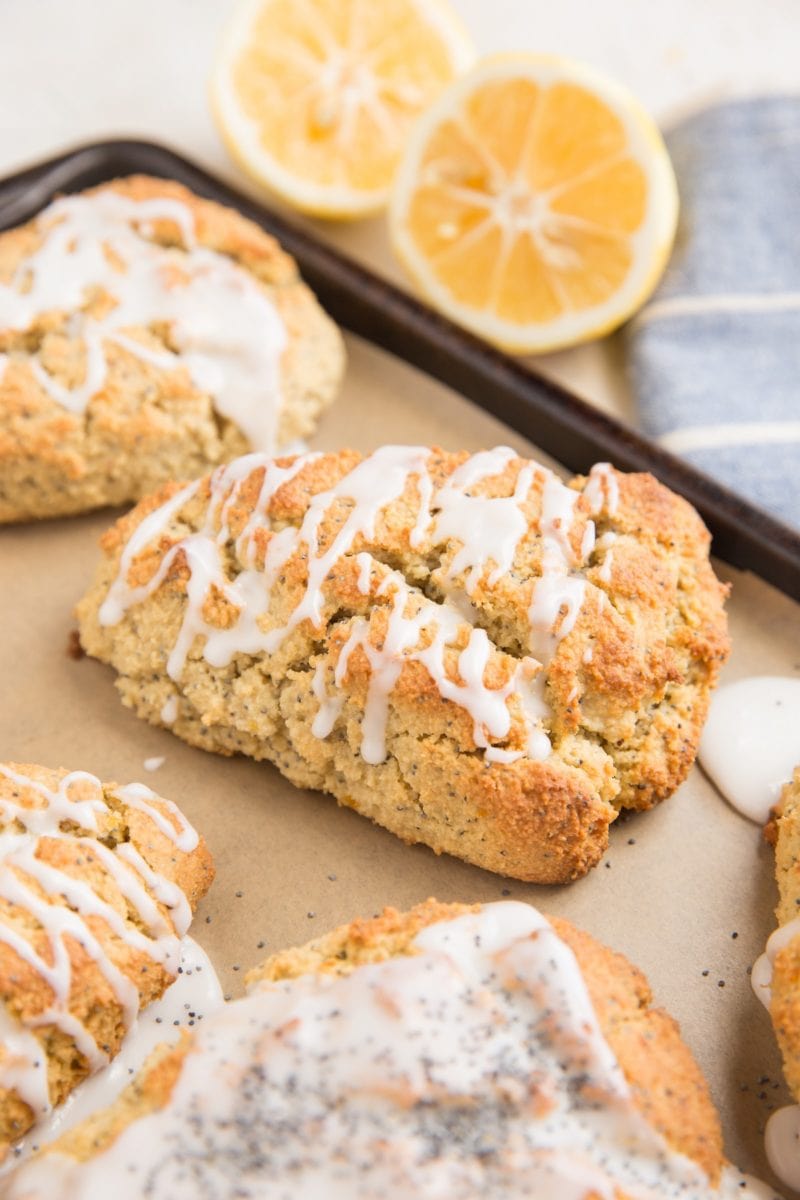 Lemon poppy seed scones on a baking sheet with lemons in the background
